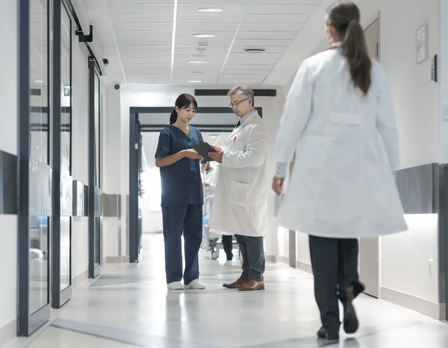 診察室で笑顔の男性医師が座っている女性患者に説明している様子。医師は白衣を着用し、右手を広げて説明しており、患者は穏やかな表情で耳を傾けている。背景には大きな窓があり、自然光が差し込んでいる。