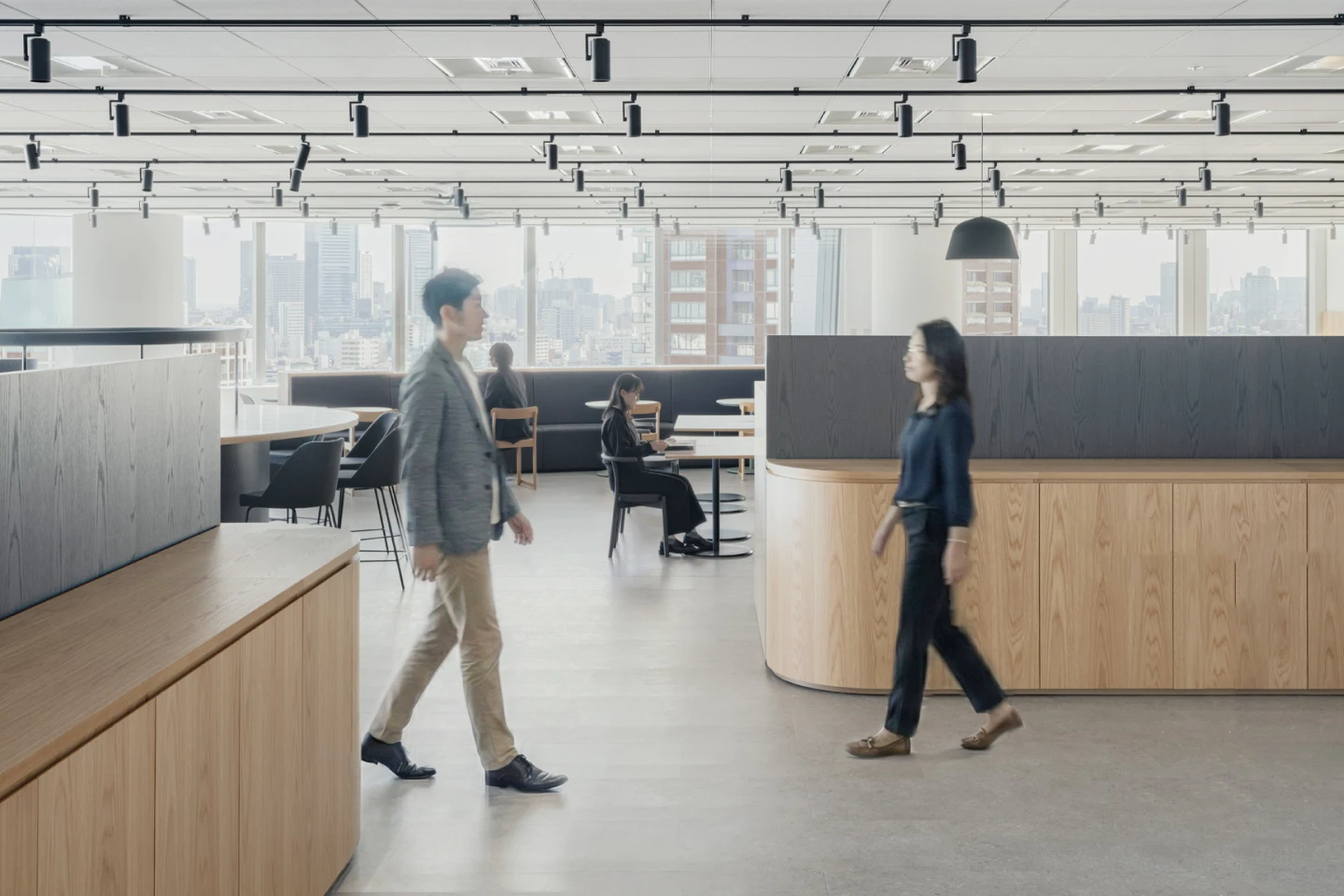 笑顔の5人のビジネスパーソンが会議室で打ち合わせをしている様子。左端に立つ男性は腕を組み、右方向を見て微笑んでいる。中央に立つ男性は白いシャツを着て、両手を前で組み、笑顔で参加者を見ている。テーブルには3台のノートパソコンが置かれ、座っている3人の男女は皆笑顔で、中央の男性の方を見ている。明るく開放的な空間で、活発な議論が行われているような雰囲気。